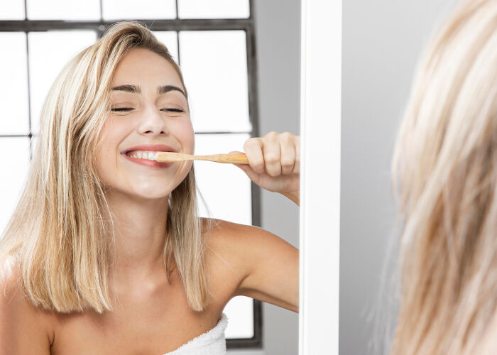 Young woman brushing teeth in front of mirror, illustrating common daily life hacks that seem clever but add extra work.