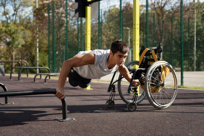 Young man with disabilities doing push-ups outdoors next to his wheelchair, demonstrating strength and resilience.