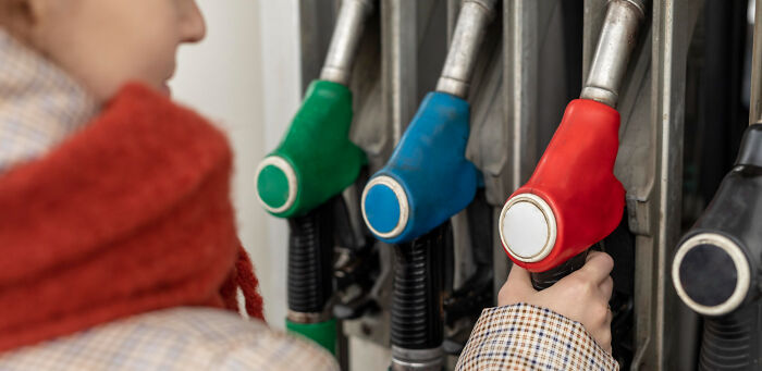 Person holding a red gas pump nozzle at a fuel station, highlighting long grudges and reasons behind them.