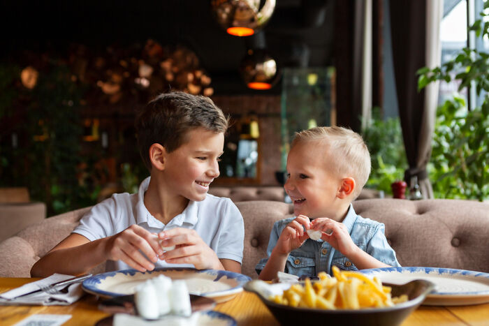 Two young boys smiling at each other while sitting at a table for two in a restaurant setting.