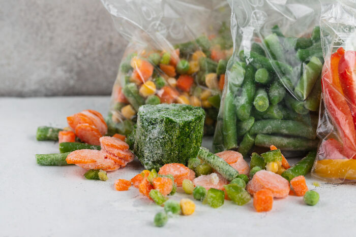 Frozen mixed vegetables in plastic bags and loose, illustrating health hacks involving frozen food tips.