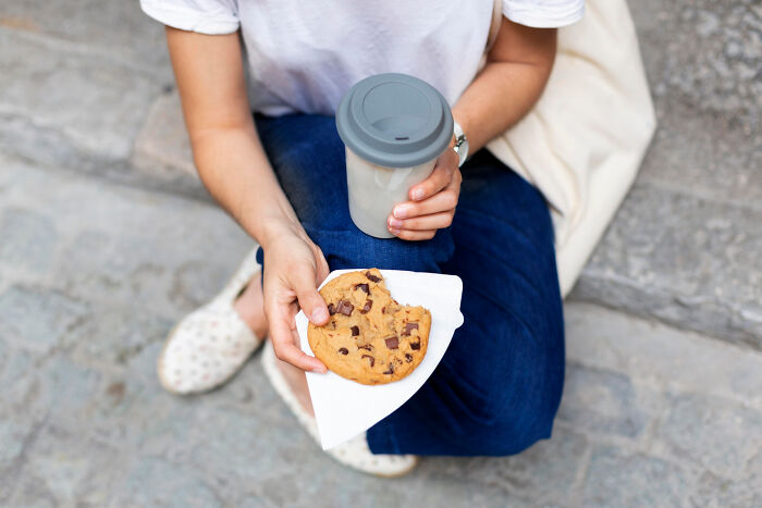 Person sitting on steps holding a coffee cup and a chocolate chip cookie, illustrating a break during moving tasks.