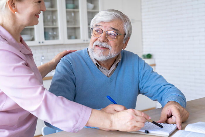 Elderly man with dementia sharing a lighthearted moment with a caregiver during a casual conversation at home.