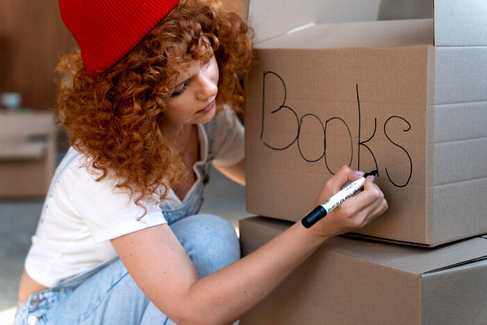 Woman with curly hair and red beanie labeling moving boxes, demonstrating tips for zip-line your boxes out during a move.