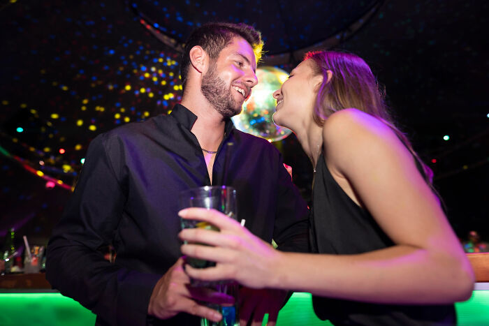 Young man and woman smiling and talking in a colorful nightclub setting, capturing unfiltered and funny dementia moments.