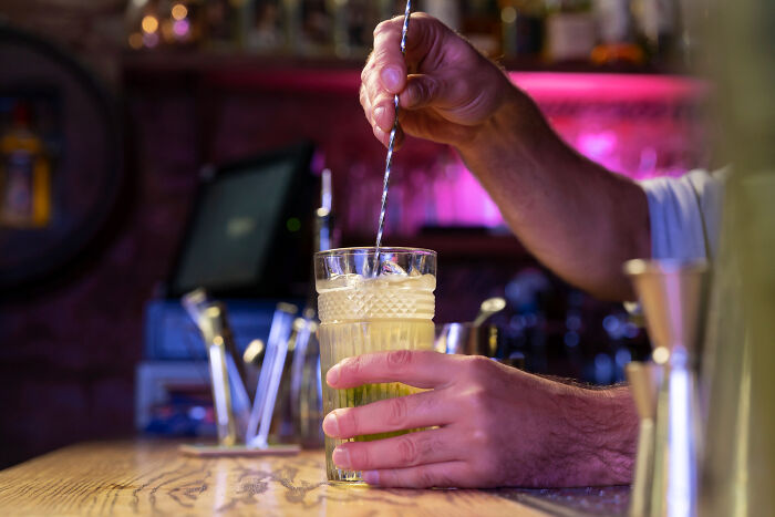 Bartender stirring a cocktail behind the bar, illustrating tales from restaurant staff about bills and money issues.