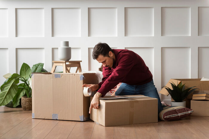 Man sealing cardboard boxes while packing, illustrating moving advice to zip-line your boxes out for easier relocation.