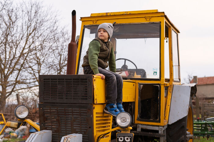 Young child sitting on an old yellow tractor outdoors, capturing a candid moment related to dementia patient stories.