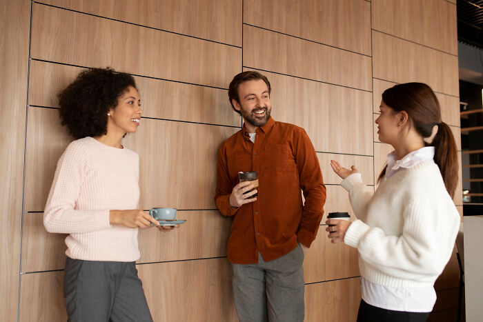 Three colleagues chatting and drinking coffee in a modern office, discussing life hacks that made people realize extra work.