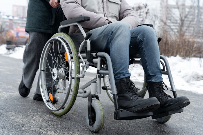 Person in a wheelchair being pushed outside on a cold day illustrating people with disabilities enduring rude and ableist treatment.