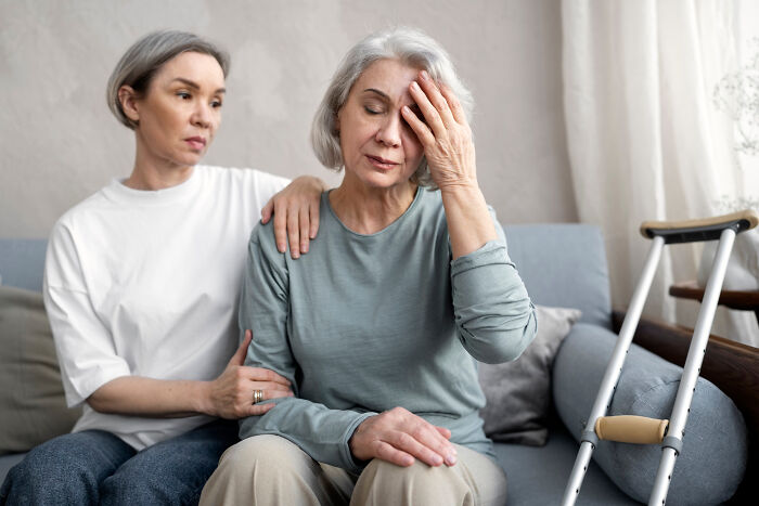 Caregiver comforting a patient with dementia showing emotional distress, sitting on a couch next to crutches.