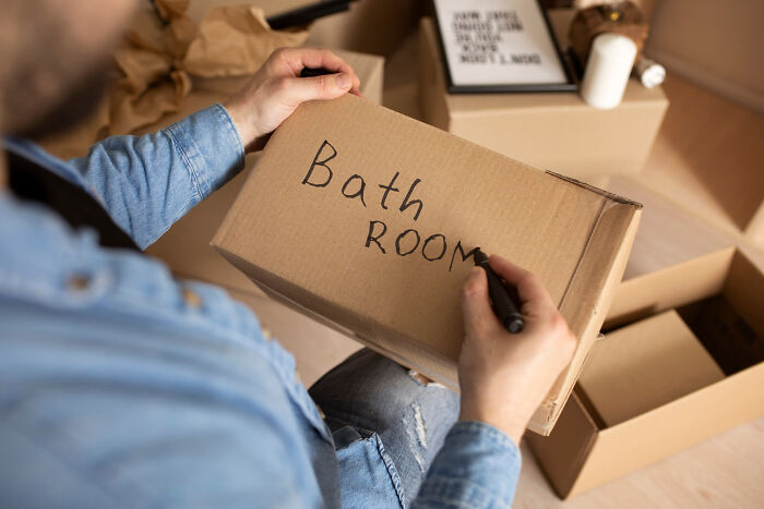 Person labeling a cardboard box with bathroom text, preparing for moving and zip-line your boxes out efficiently.