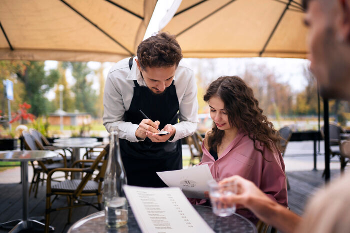 Waiter taking order from woman at outdoor cafe, capturing a hilariously painful moment misreading social cues.