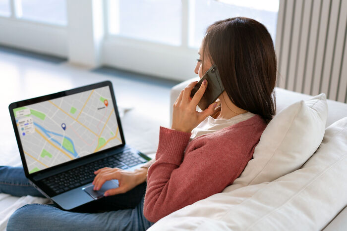 Woman using laptop with map on screen and talking on phone, illustrating unhinged stalking behavior concept.