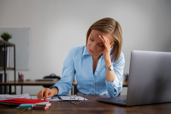 Stressed woman sitting at desk with laptop, highlighting unfair relationships caused by gender roles in the workplace.