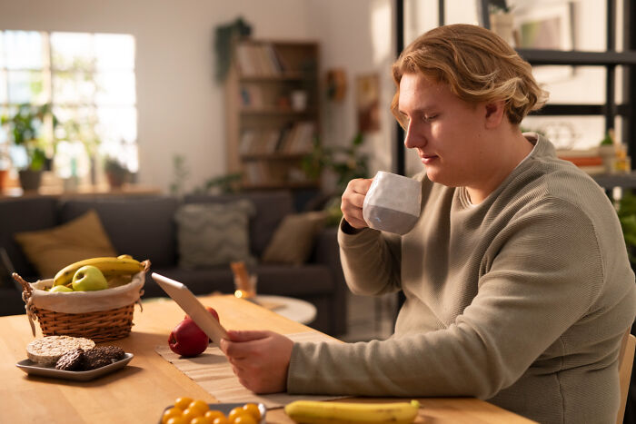 Young man drinking coffee while reading about terrifying medical conditions that can end without showing symptoms at home.