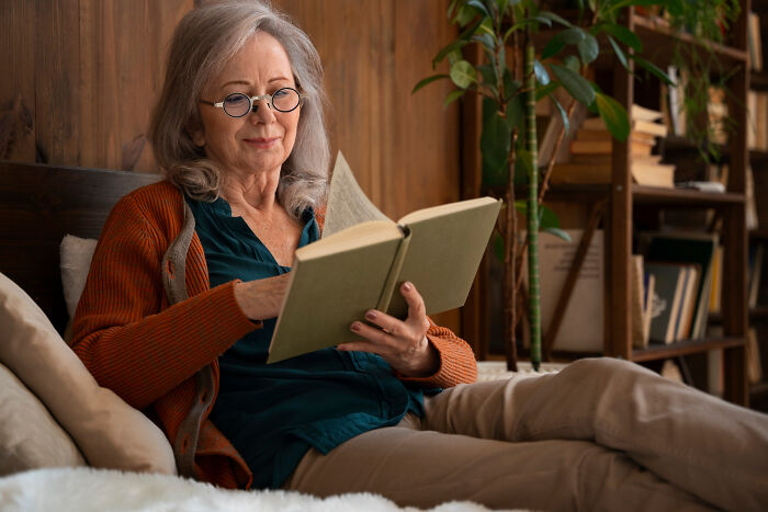 Elderly woman reading a book calmly in a cozy home setting, reflecting moments of unfiltered and funny dementia patient quotes.
