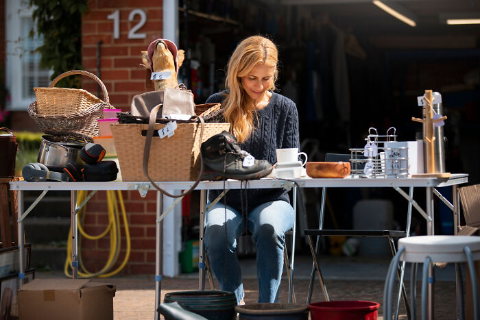 Woman organizing and pricing items for a sale outside a house, illustrating creative moving and packing advice with boxes.