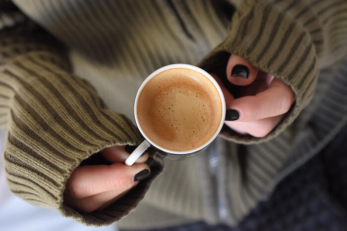 Person wearing a green sweater holding a cup of coffee, illustrating a relaxed moment amid moving boxes and advice.