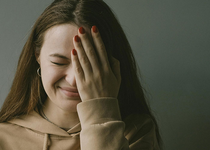 Young woman covering her face in embarrassment, reflecting a moment when a kid embarrassed their mom deeply.