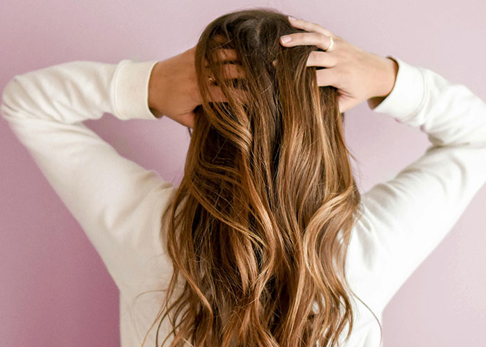 Woman with long brown hair holding her head from the back, illustrating regret after a cosmetic procedure done.