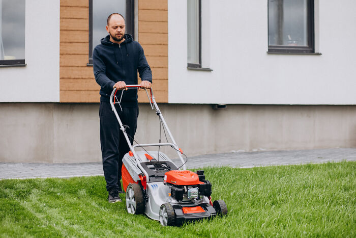 Man mowing lawn outside house, illustrating unfair gender roles in relationships and household chores.