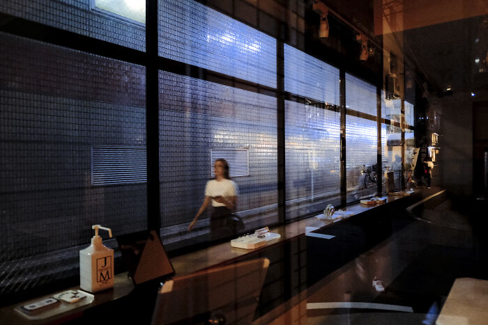 Blurred figure walking outside a window reflecting interior details, capturing life’s unexpected moments in stunning street photography.