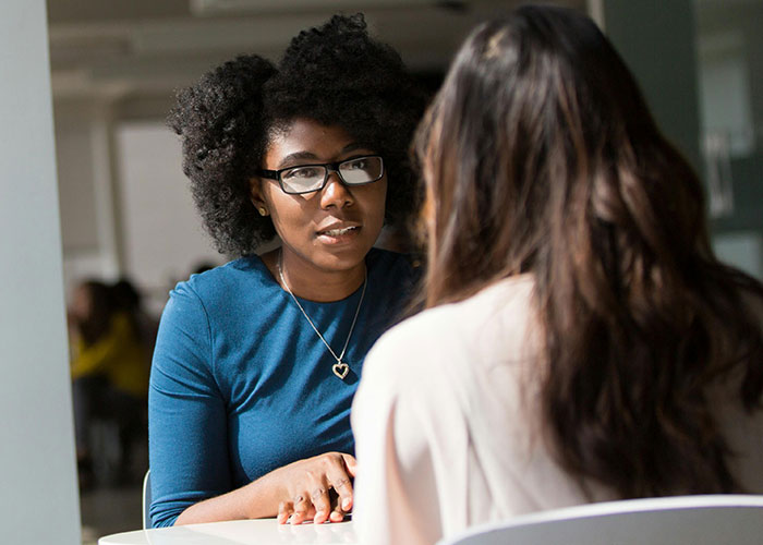 Two women having a focused conversation indoors, illustrating life hacks people discovered accidentally and still use.