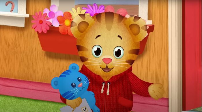 Animated tiger character in a red hoodie holding a blue stuffed animal outside a house with flower boxes SEO keywords.