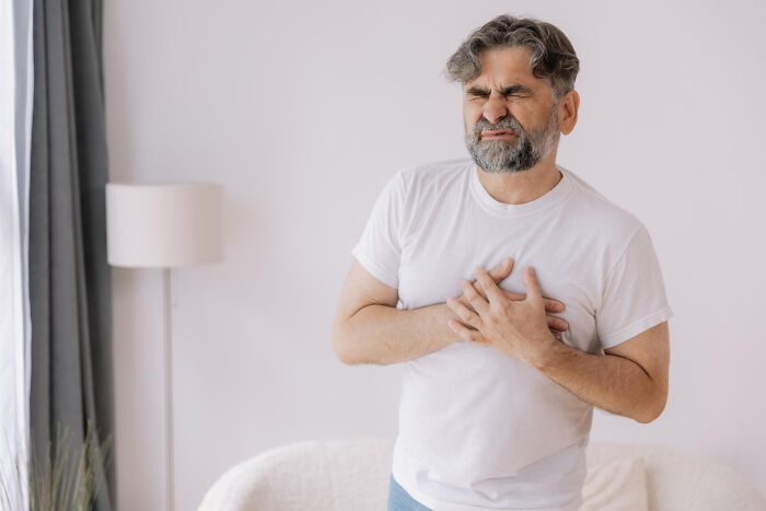Man in white shirt clutching chest in pain, illustrating terrifying medical conditions with no symptoms.
