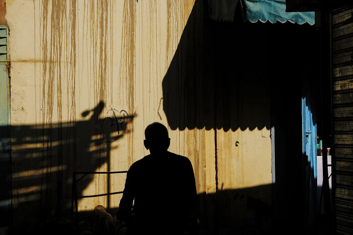 Silhouette of a person against a wall with shadows, showcasing stunning street photography capturing unexpected moments.