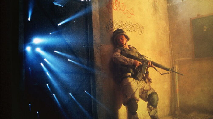 Soldier holding a rifle leaning against a wall in a dimly lit room from a movie based on true stories.