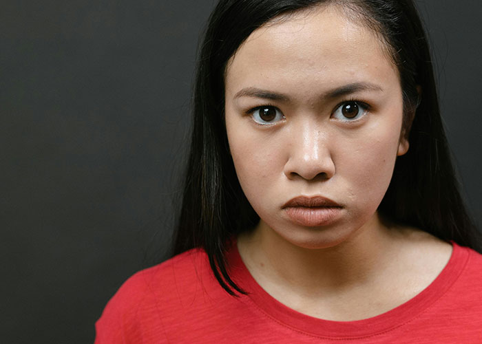 Young woman with a serious expression wearing a red shirt, representing creepy things women said or did to men.