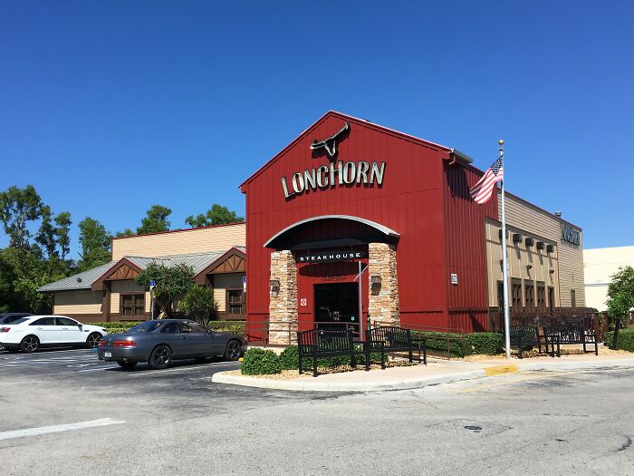 Exterior of LongHorn Steakhouse with parked cars on a sunny day, illustrating restaurant staff tales about bill and payment issues.