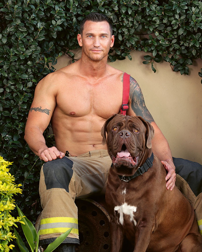 Shirtless firefighter with tattoos sitting outdoors next to a large brown dog, showcasing heroic firefighters and adorable dogs.