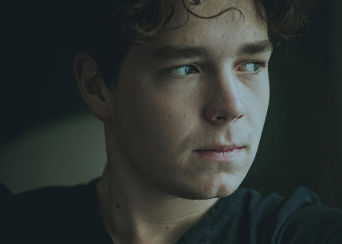 Young man looking pensively out of a window, illustrating creepy things women said or did that left men horrified.