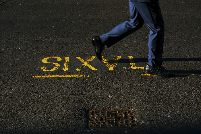 Person walking past a yellow taxi sign on the street pavement, capturing stunning street photography moments.