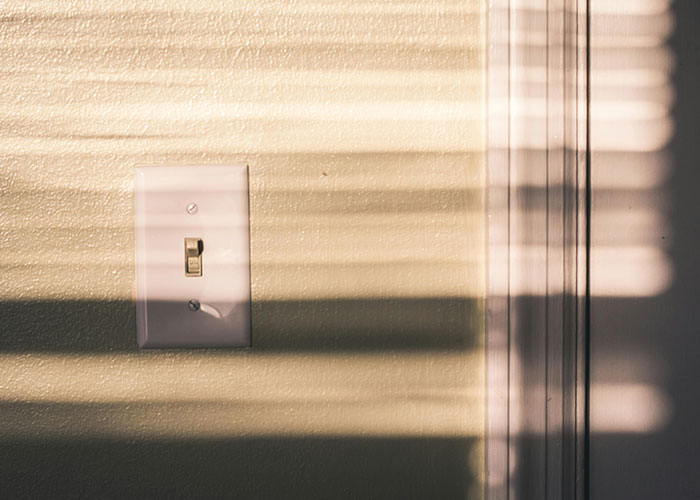 Light switch on textured wall with shadows from blinds creating a pattern, illustrating simple life hacks discovered accidentally.