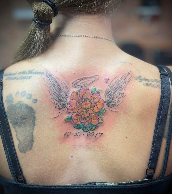 Colorful flower tattoo with wings and a halo on the upper back, one of the unusual tattoos people allow on their bodies.