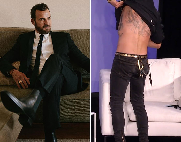 Man in a black suit sitting on a couch next to a person showing back tattoos while lifting their shirt indoors.