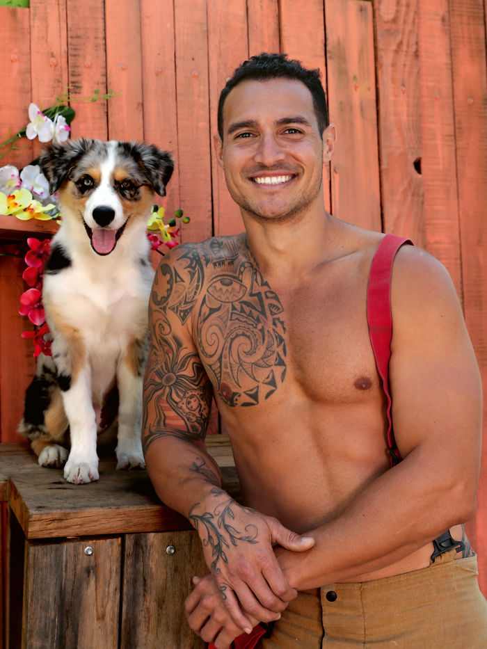 Shirtless firefighter with intricate tattoos smiling beside an adorable dog, featured in Australian calendar photos.