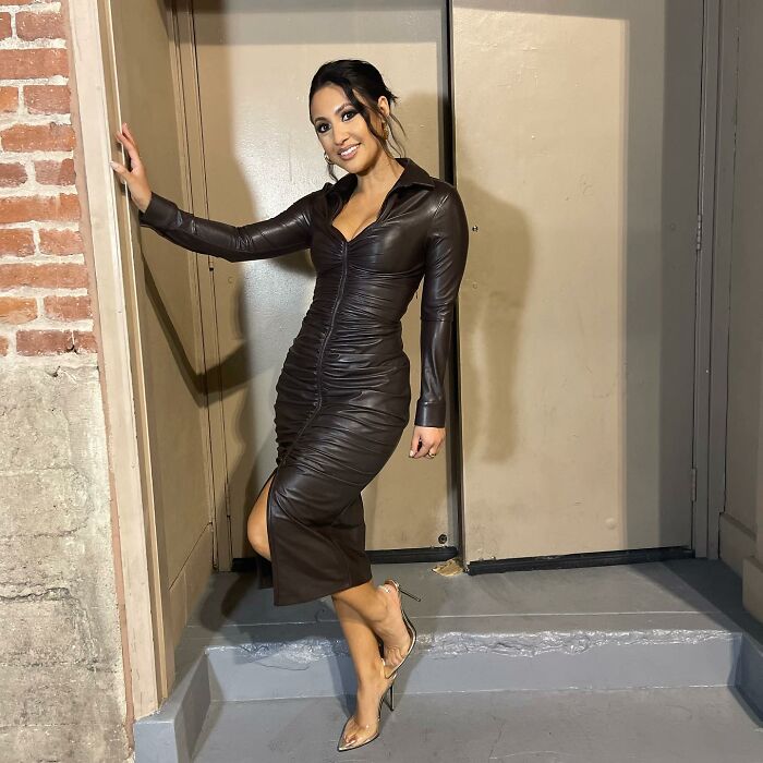 Woman in a fitted brown leather dress and heels posing by a doorway, fans suspicious of Selena Gomez's kidney donor.