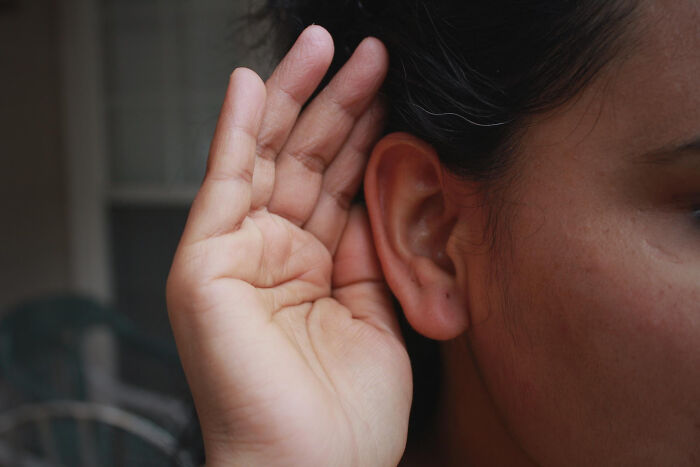 Close-up of a person holding their hand to their ear symbolizing listening to people with disabilities sharing their experiences.