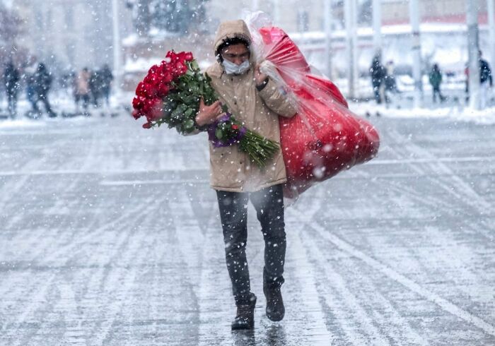 Person carrying red roses and a large red sack walking through snow on Istanbul streets during winter weather.