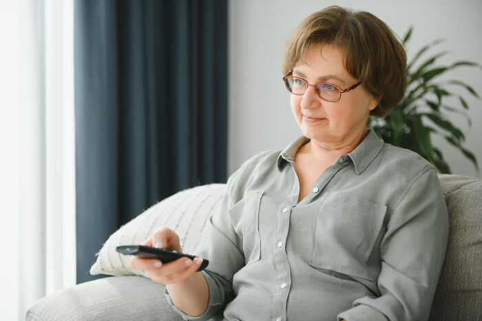 Middle-aged woman struggling with technology skills while trying to use a remote control on a couch.