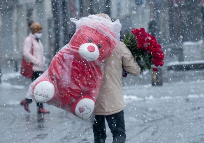 Person carrying red roses and a large red sack walking through snow on Istanbul streets during winter weather.