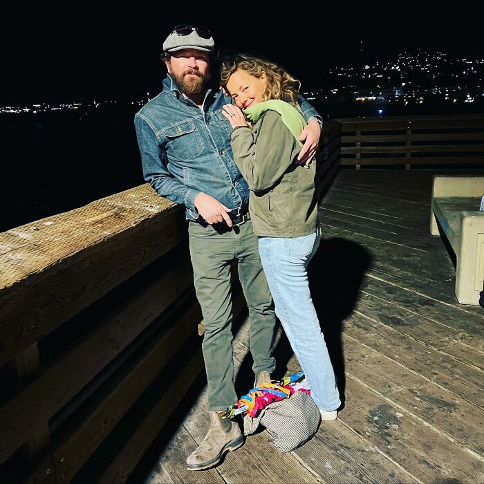 Bijou Phillips and Danny Masterson standing on a wooden pier at night, dressed casually in jackets and jeans.