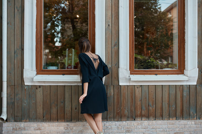 Woman in black dress peeking through a window of a wooden house, illustrating unhinged stalking behavior stories.
