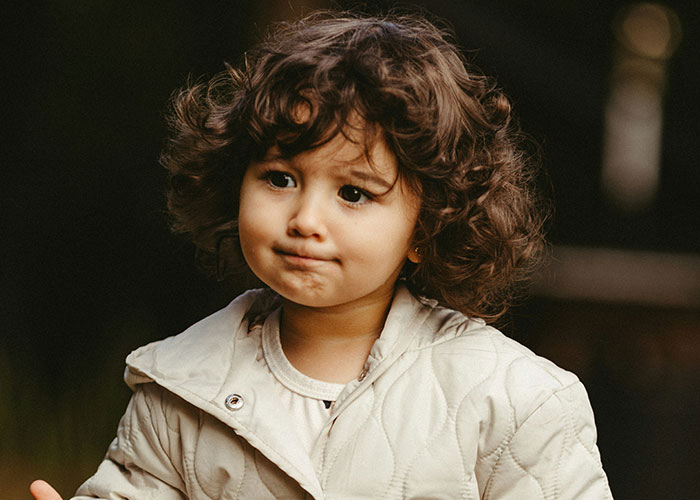 Young child with curly hair making a thoughtful face, capturing moments of kids’ hilarious and mortifying things said or done.