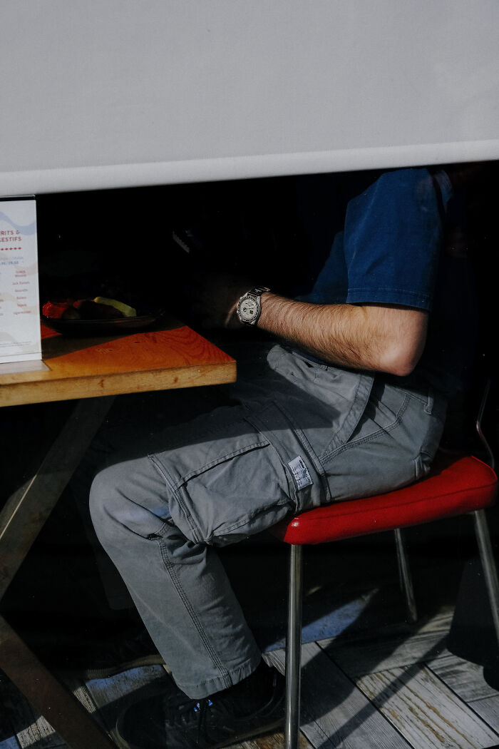 Man sitting at a wooden table wearing gray cargo pants and a watch, captured in a stunning street photography shot.